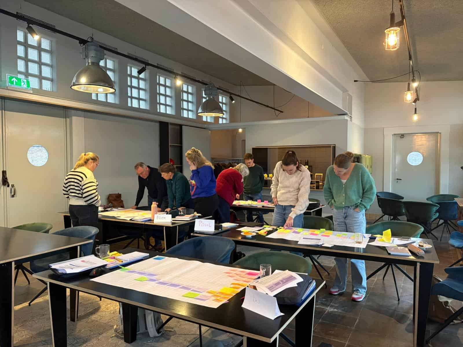 Deelnemers werken aan tafels met ontwerpvellen en gekleurde post-its
